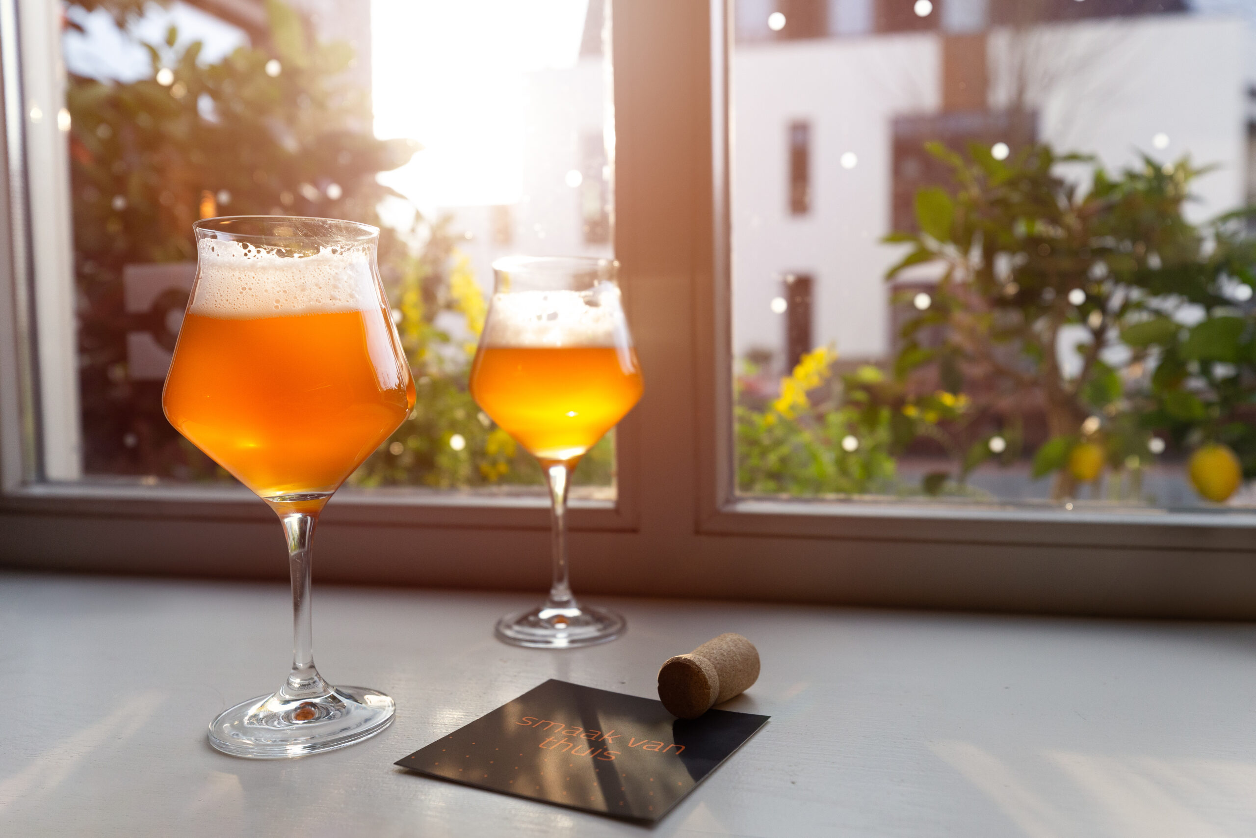 Speciaal ontworpen fles Carré De Witbier met mango, met een levendige illustratie van een verkochte woning, geplaatst tegen de achtergrond van het kantoor.